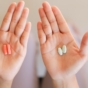 Close-up of two hands, each holding two pills of the same type.