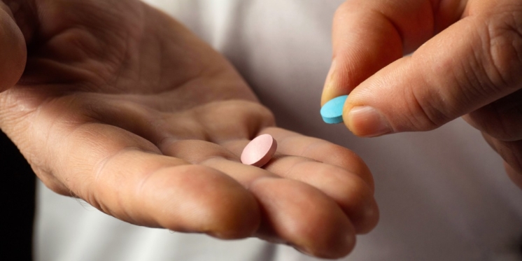 Person taking two different types of pills.