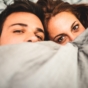 couple peek over bed sheets