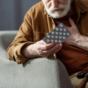older man holding medication and chest