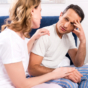 woman consoling man on edge of bed