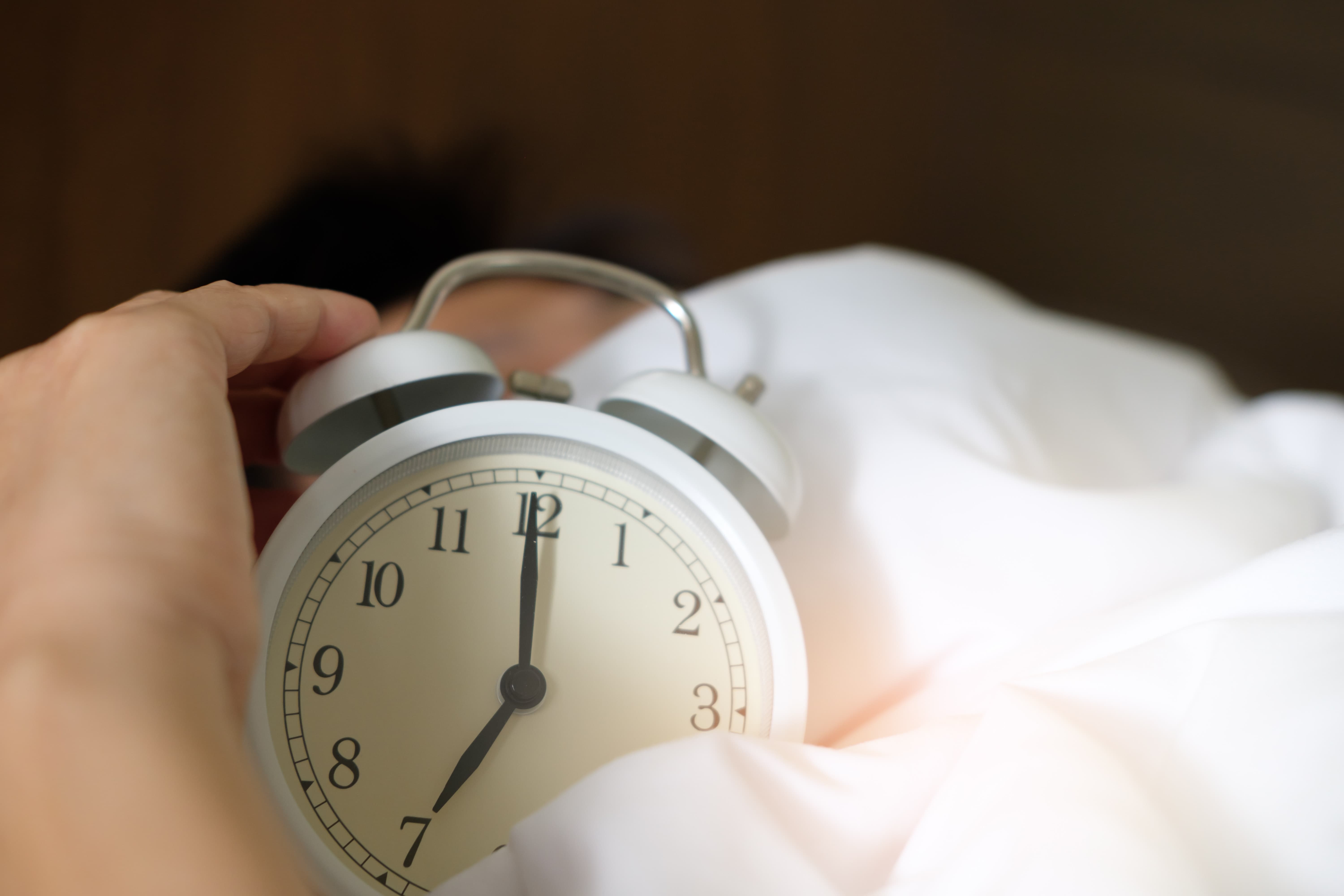 An alarm clock on a bed with a hand on it