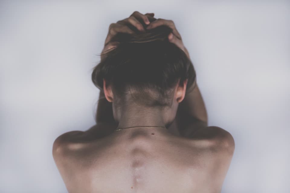 The back of a woman who is holding her head as if she is in a lot of pain