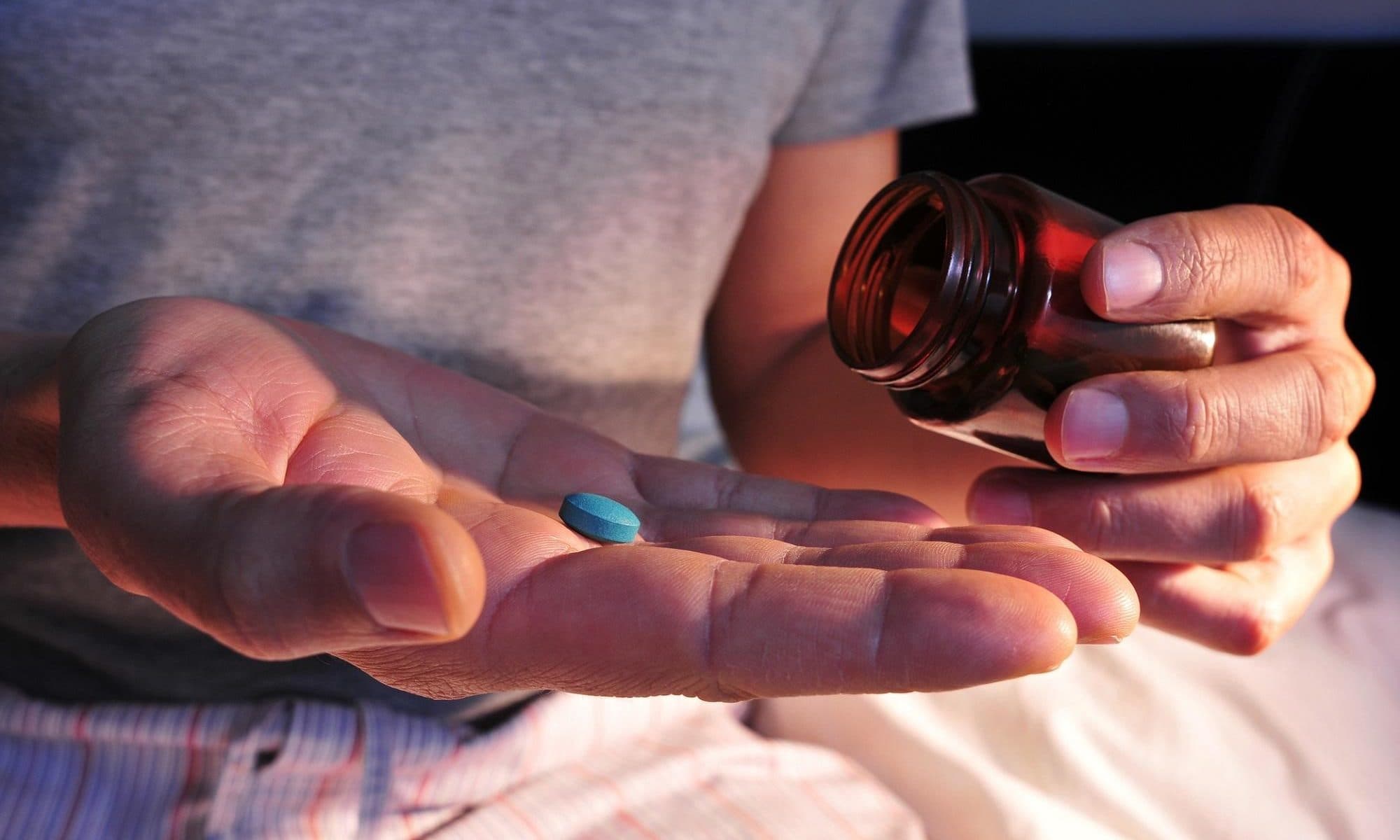 A man taking a blue tablet into his hand out of a medicine jar