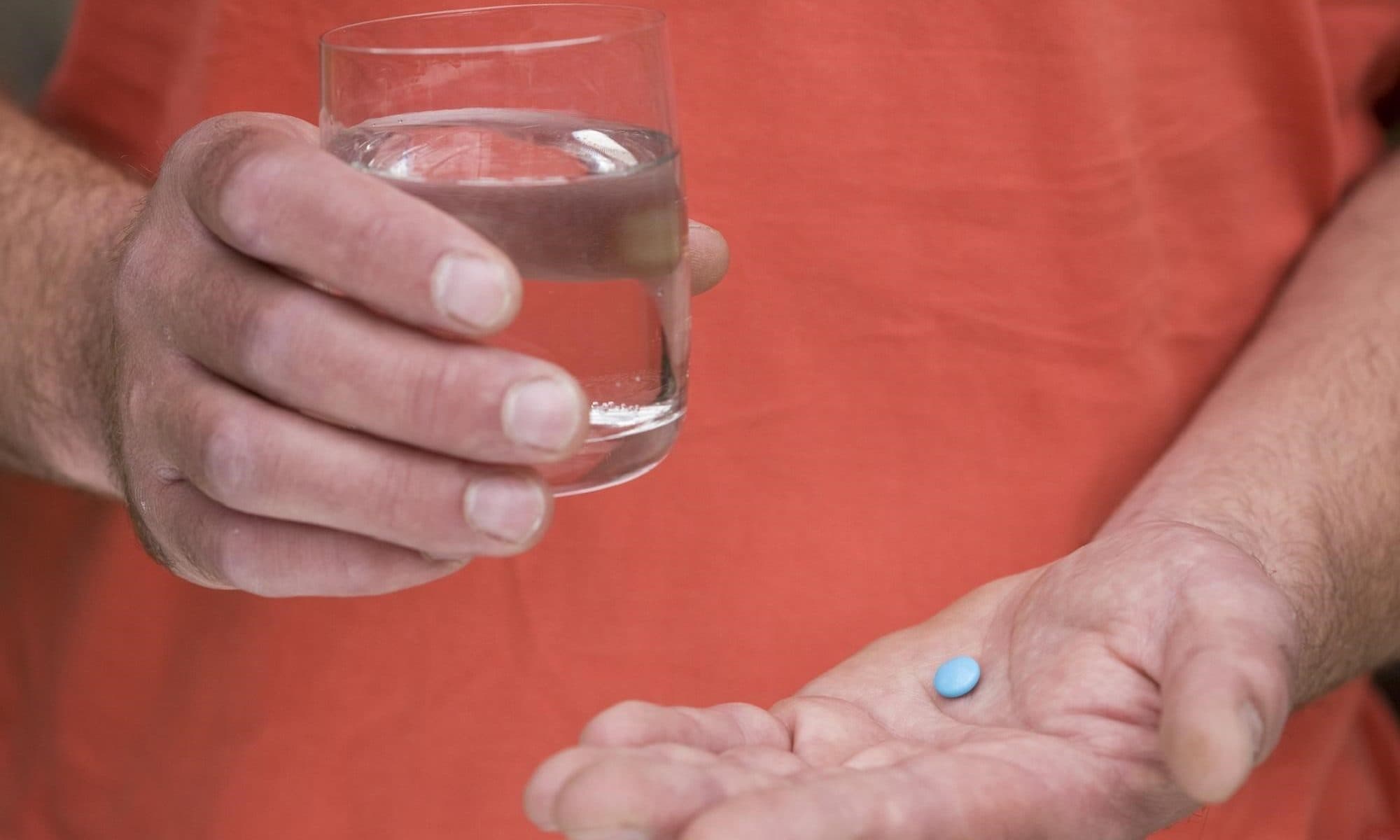 A man holding a glass of water in one hand, and a viagra pill in the other hand