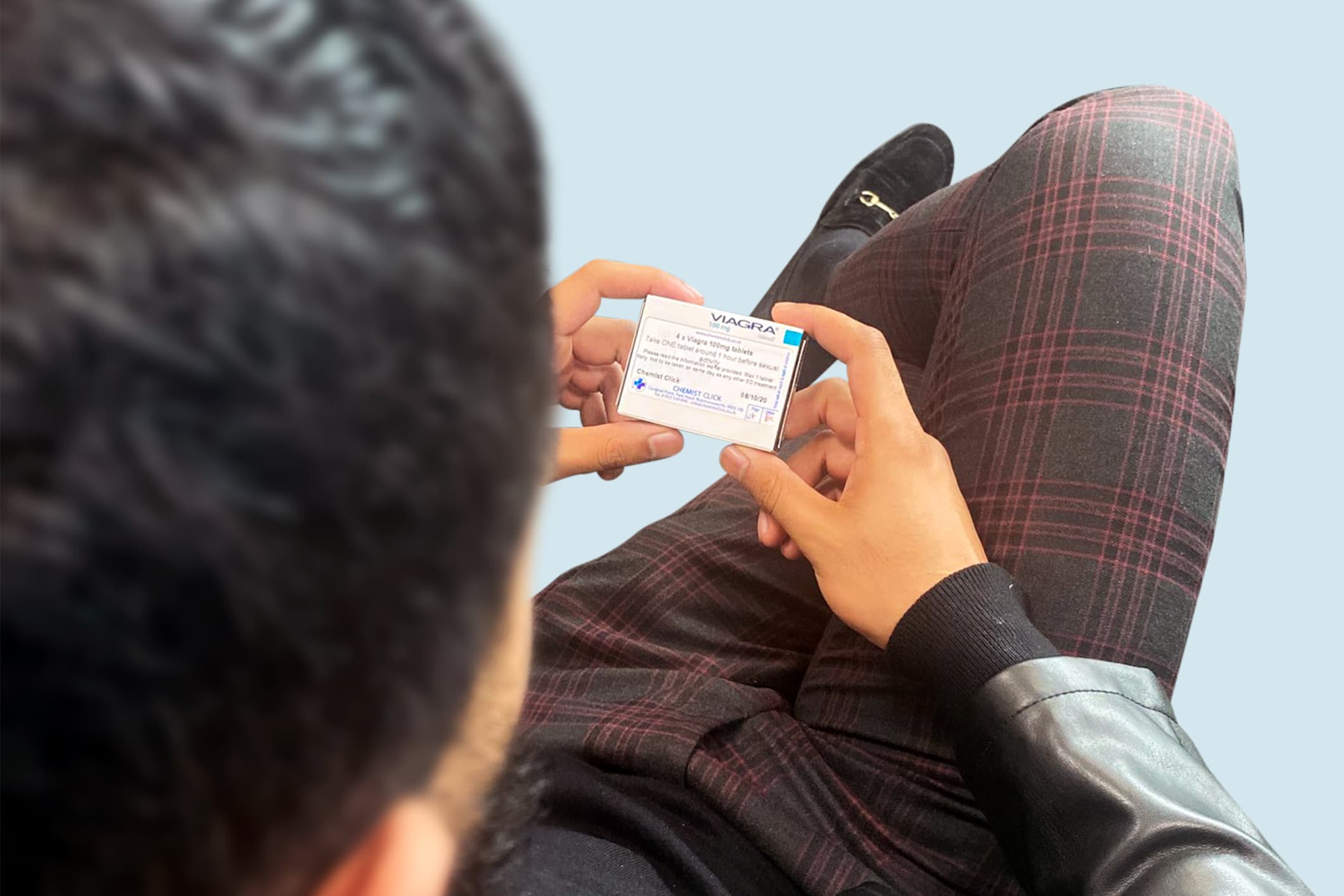 A man sitting down with his legs crossed reading the pharmacy label on a box of Viagra