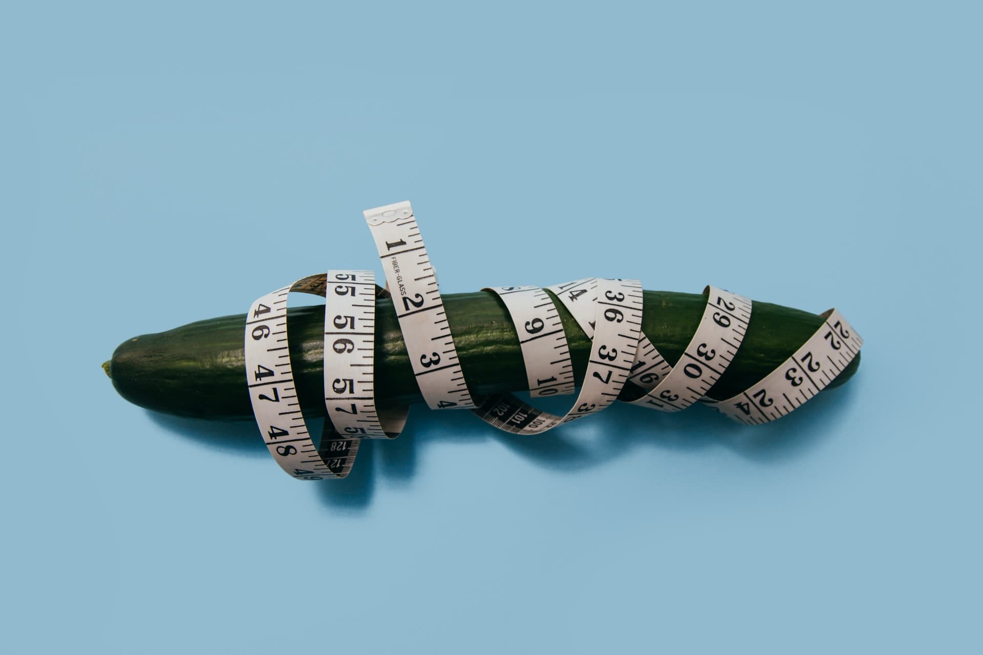 Cucumber with a measuring tape wrapped around it on a blue background