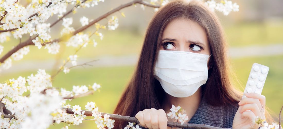 Woman holding hayfever tablets next to blossoming tree