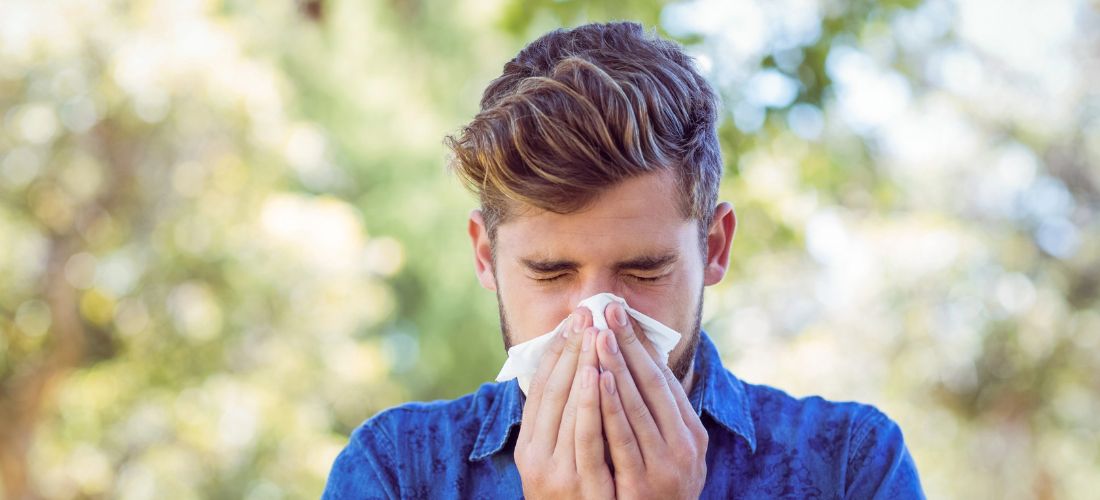 Man sneezing into tissue outdoors