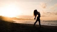 woman performing yoga on the beach with sun setting in the background